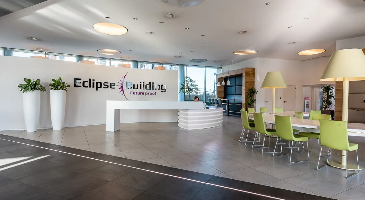 Moderne en lichte ontvangsthal van het Eclipse Building met balie, zithoek en groene accenten.